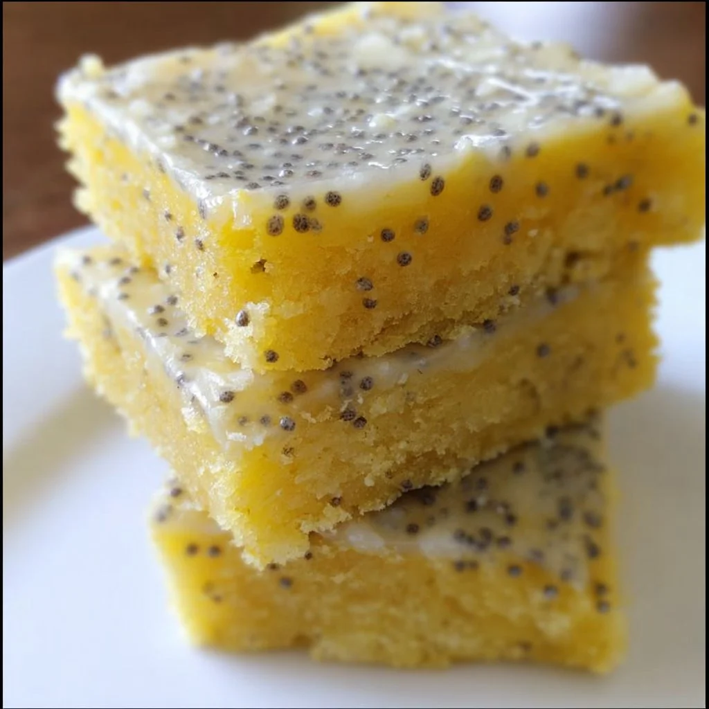 Glazed lemon poppy seed bars on a white plate garnished with lemon zest.