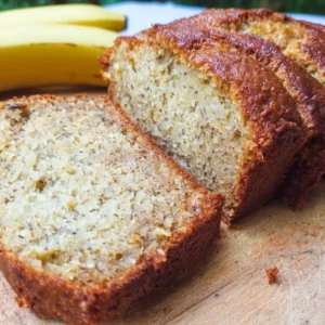 A slice of super moist banana bread on a wooden cutting board