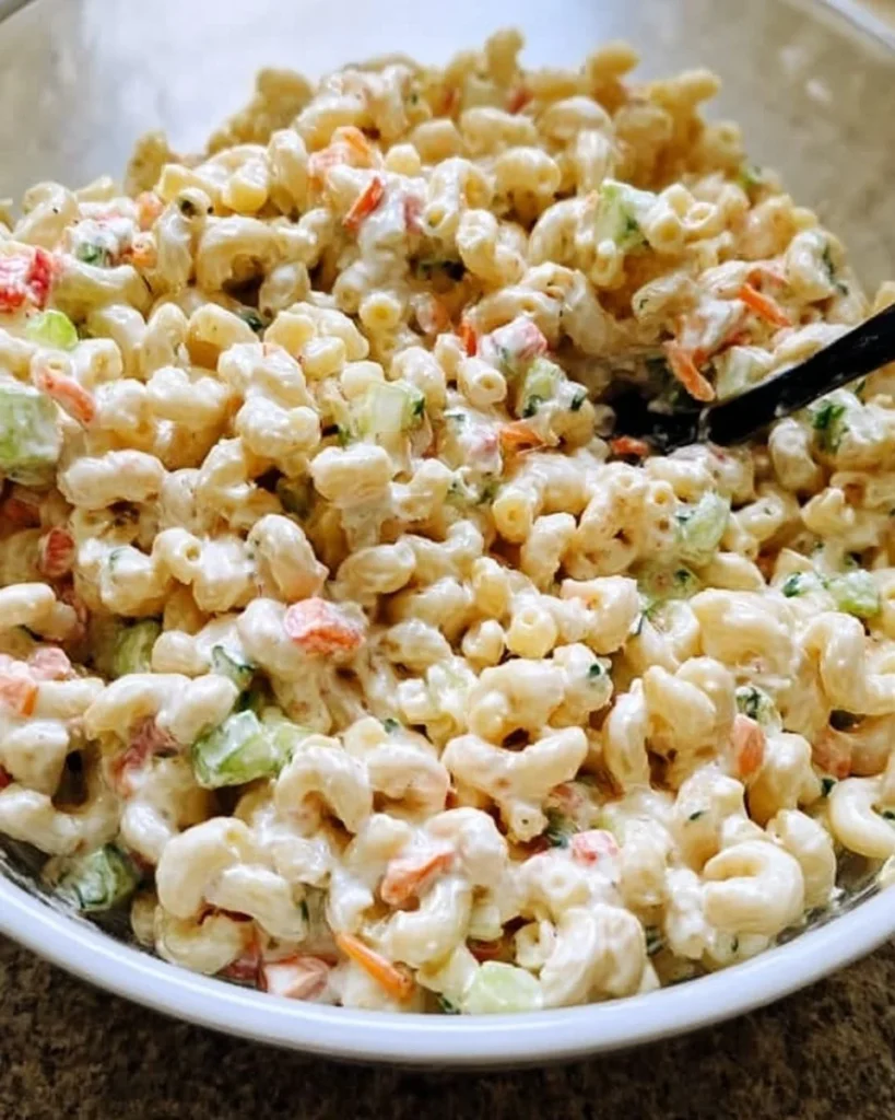 Creamy macaroni salad in a bowl, garnished with herbs and vegetables.