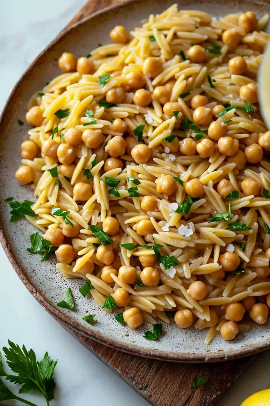 A vibrant bowl of orzo pasta with chickpeas garnished with herbs